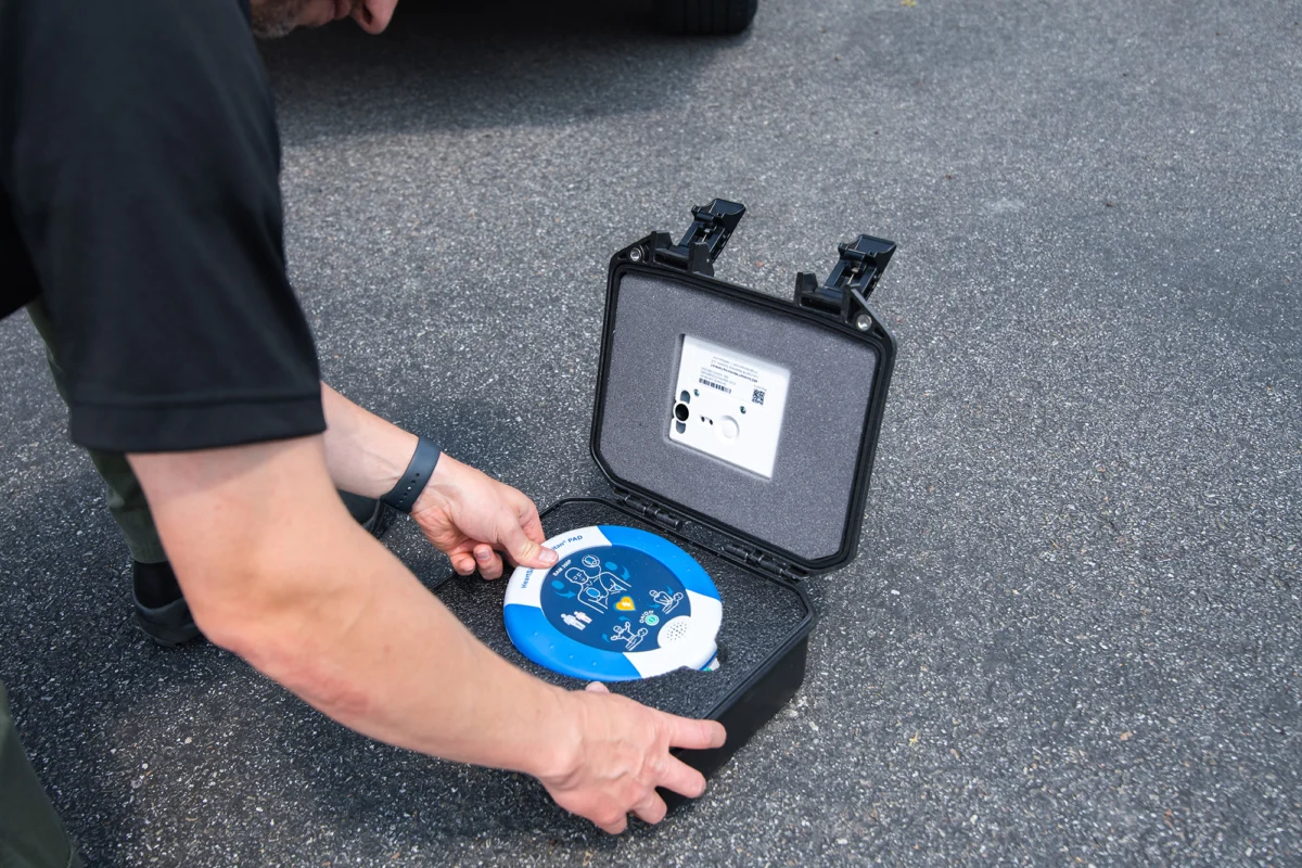 A person checking a HeartSine samaritan PAD AED in a hard carry case with an AED Sentinel monitor in the lid